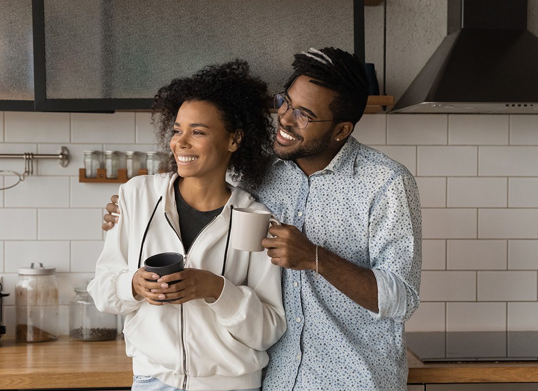 Personal Insurance - Happy Couple Standing Together in Their Kitchen Having Coffee